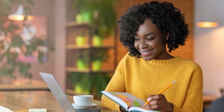 Woman looking at her laptop and writing in her notebook